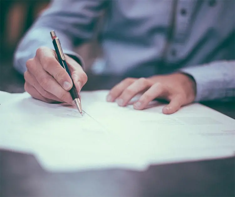 Person signing an official document with a pen at a desk, representing record-keeping, approvals, and administrative processes in local government.