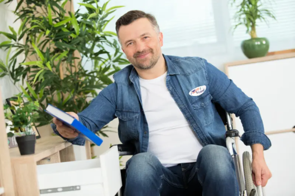 Man using a wheelchair wearing an "I Voted" sticker and holding a binder, smiling in a bright indoor setting
